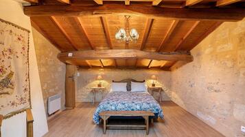 A bedroom with a wooden ceiling, a bed with a floral bedspread, two bedside lamps, and a wooden bench.
