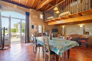 Un intérieur rustique comprenant une table à manger, des chaises, un canapé, un balcon et un mur en pierre.