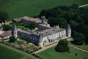 An aerial view of a large estate with multiple buildings, including a central structure with a conical roof and several cylindrical towers. - La Roseraie Guest Room with Private Terrace, Garden & Wi-Fi in Saint-Émilion (Saint-Émilion)