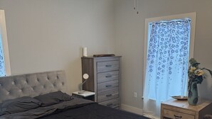 Makuuhuoneessa on sänky, yöpöytä, lipasto, kattotuuletin ja ikkuna, jossa on verhot.