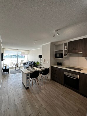 A modern kitchen with a dining area, wooden flooring, and a view through large windows. - Fabulous Apartment 2D2B Steps from the Beach - La Serena (La Serena)