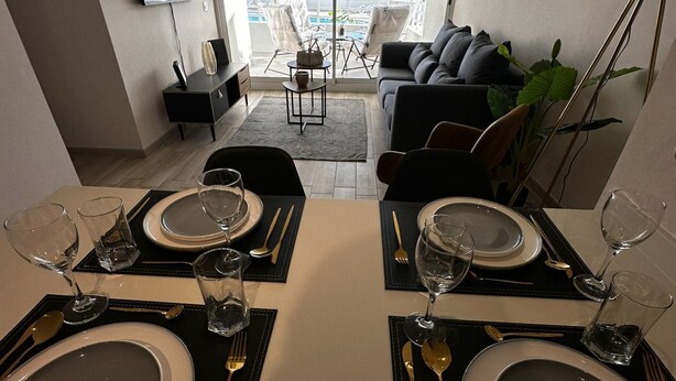 Un coin repas avec une table dressée pour deux personnes, un canapé et un téléviseur fixé au mur.