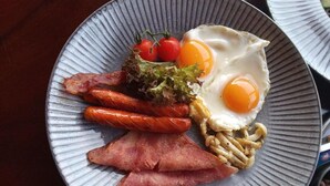 Um prato com ovos, bacon, salsichas e legumes.