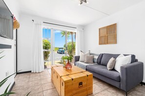 A modern living room with a grey sofa, a wooden coffee table, and a large window with a view of the outside. - Big Bay Beach Club 182 (Cape Town)