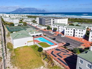 A residential area with a swimming pool, parking, and a view of the ocean. - Big Bay Beach Club 182 (Cape Town)