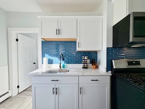 Una cocina moderna con armarios blancos, salpicadero azul, estufa de acero inoxidable y microondas negro.