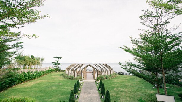 A pathway leading to a building with a unique architectural design, surrounded by well-maintained lawns and trees. - Mactan Newtown Haven (Lapu-Lapu)