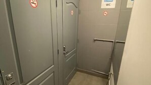 Un pasillo estrecho con puertas grises, cada una con un cartel de prohibido fumar. Un letrero en la pared derecha indica un baño.