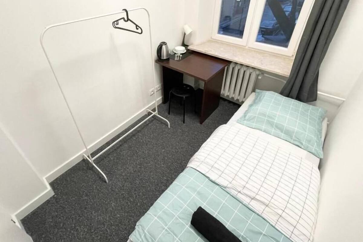 A small, tidy room with a bed, a desk, a chair, and a radiator.