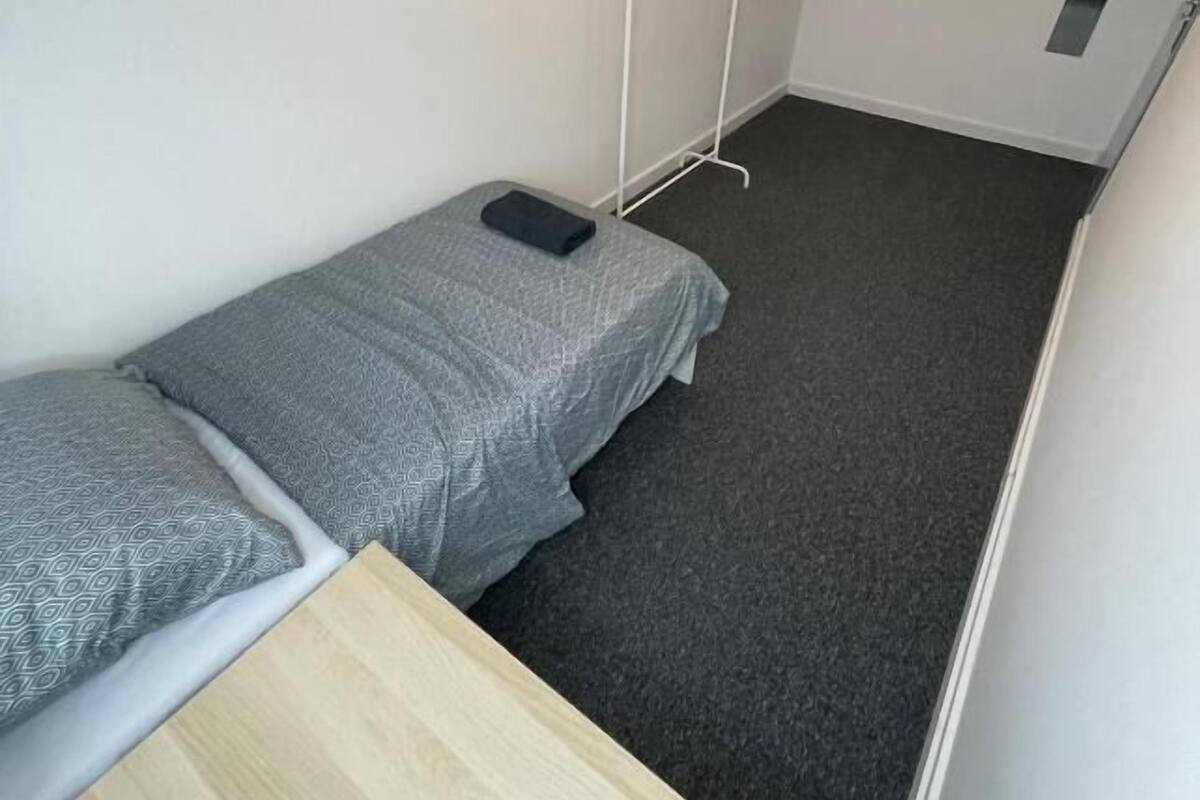 A narrow room with a single bed, a small table, and a wall-mounted drying rack.