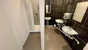 Un baño con ducha, dos lavamanos y un inodoro.