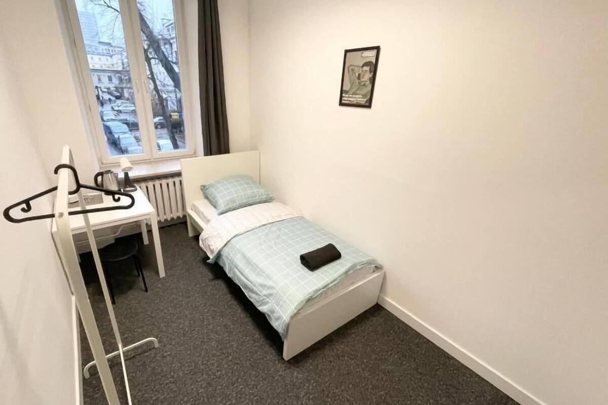 A small, neatly arranged bedroom with a single bed, a desk, and a radiator.