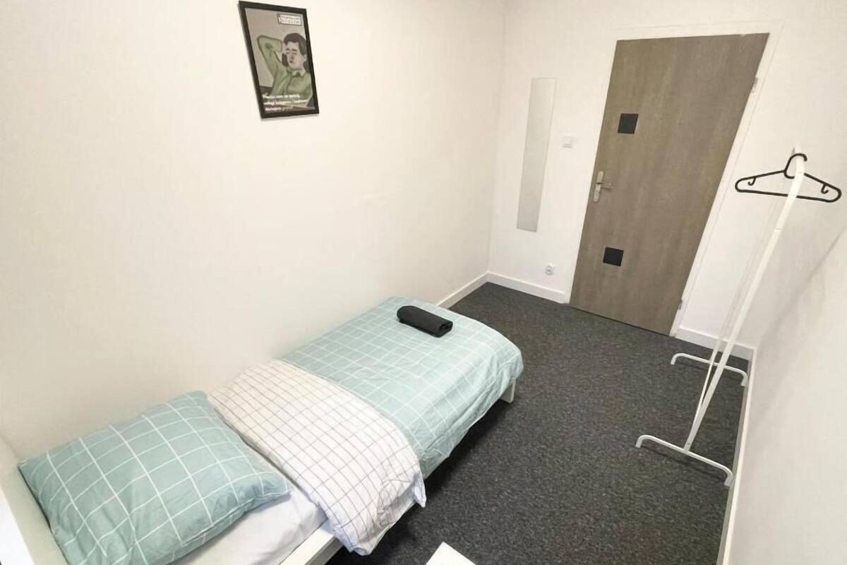 A small, single-bed room with a grey carpet, a white wall, and a door.