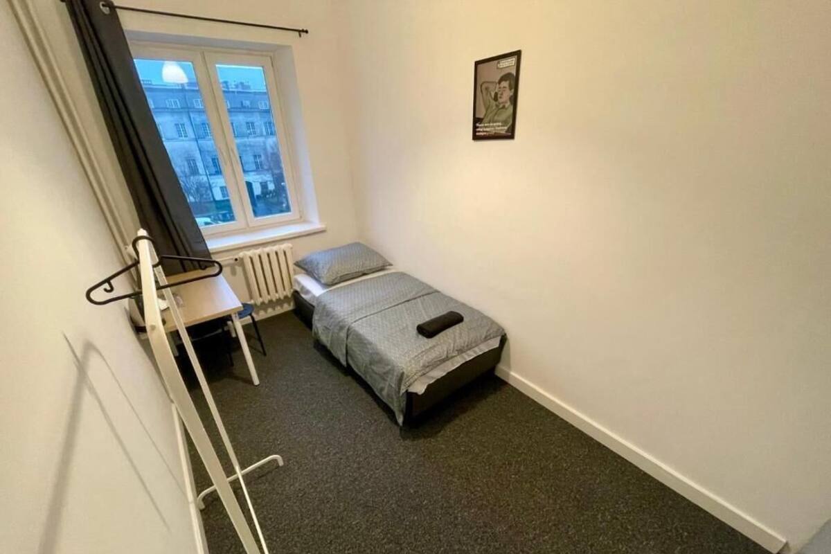 A small, compact room with a single bed, a radiator, a window with curtains, and a poster on the wall.