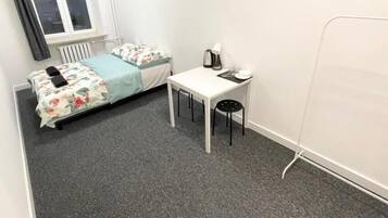 Et lille, rent værelse med en enkeltseng, et hvidt bord og en stol.