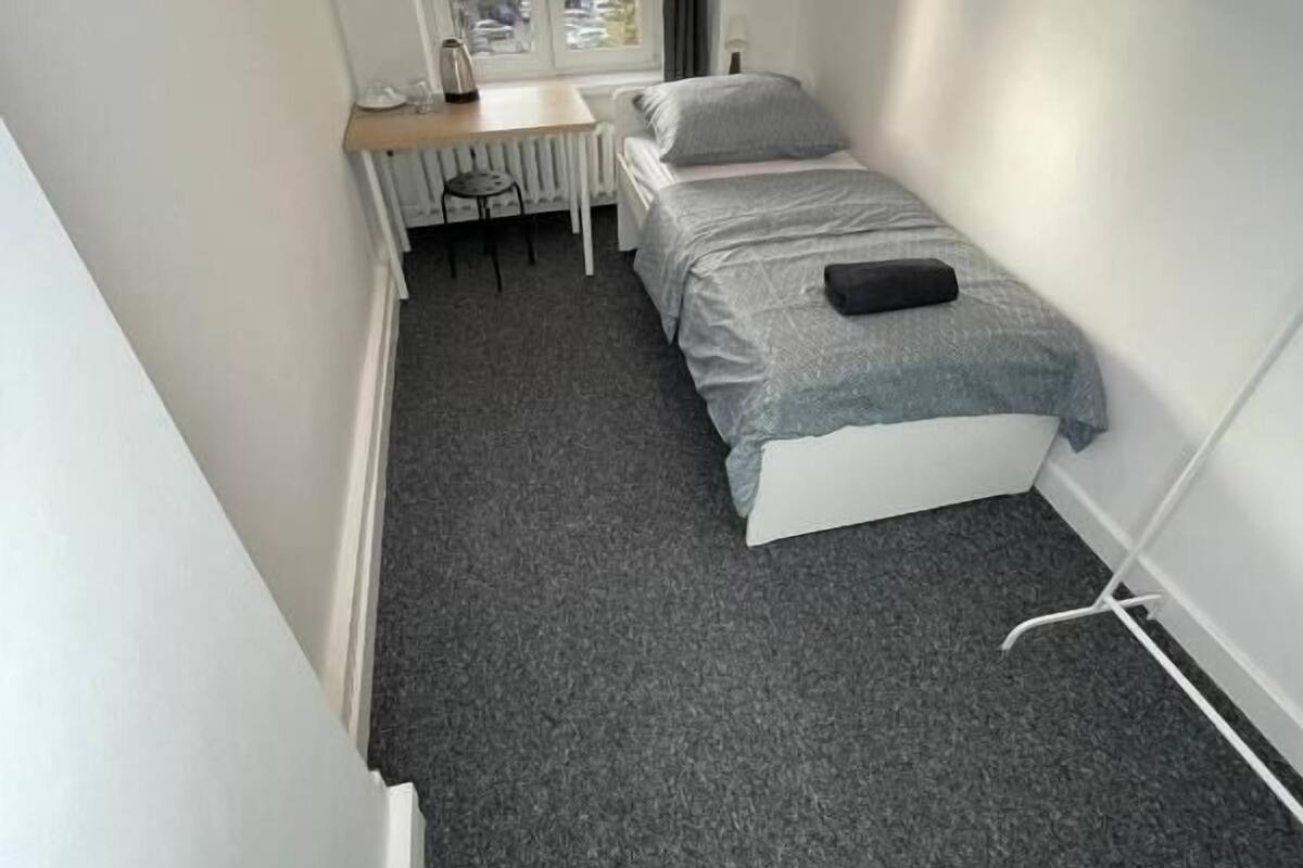 A small, narrow room with a bed, a desk, and a chair.