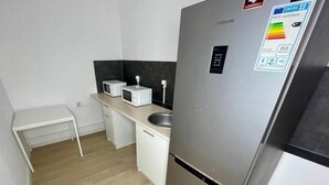 Una cocina compacta con refrigerador de acero inoxidable, microondas y un lavamanos pequeño.