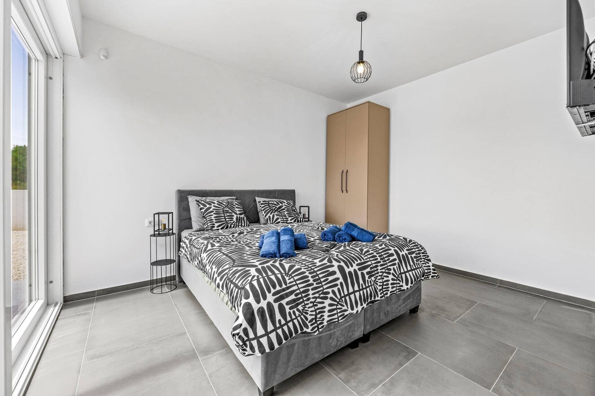 Une chambre moderne avec un grand lit, une armoire et un luminaire suspendu.