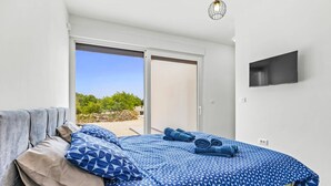 Una camera da letto con un letto, cuscini, una televisione e vista sul verde.