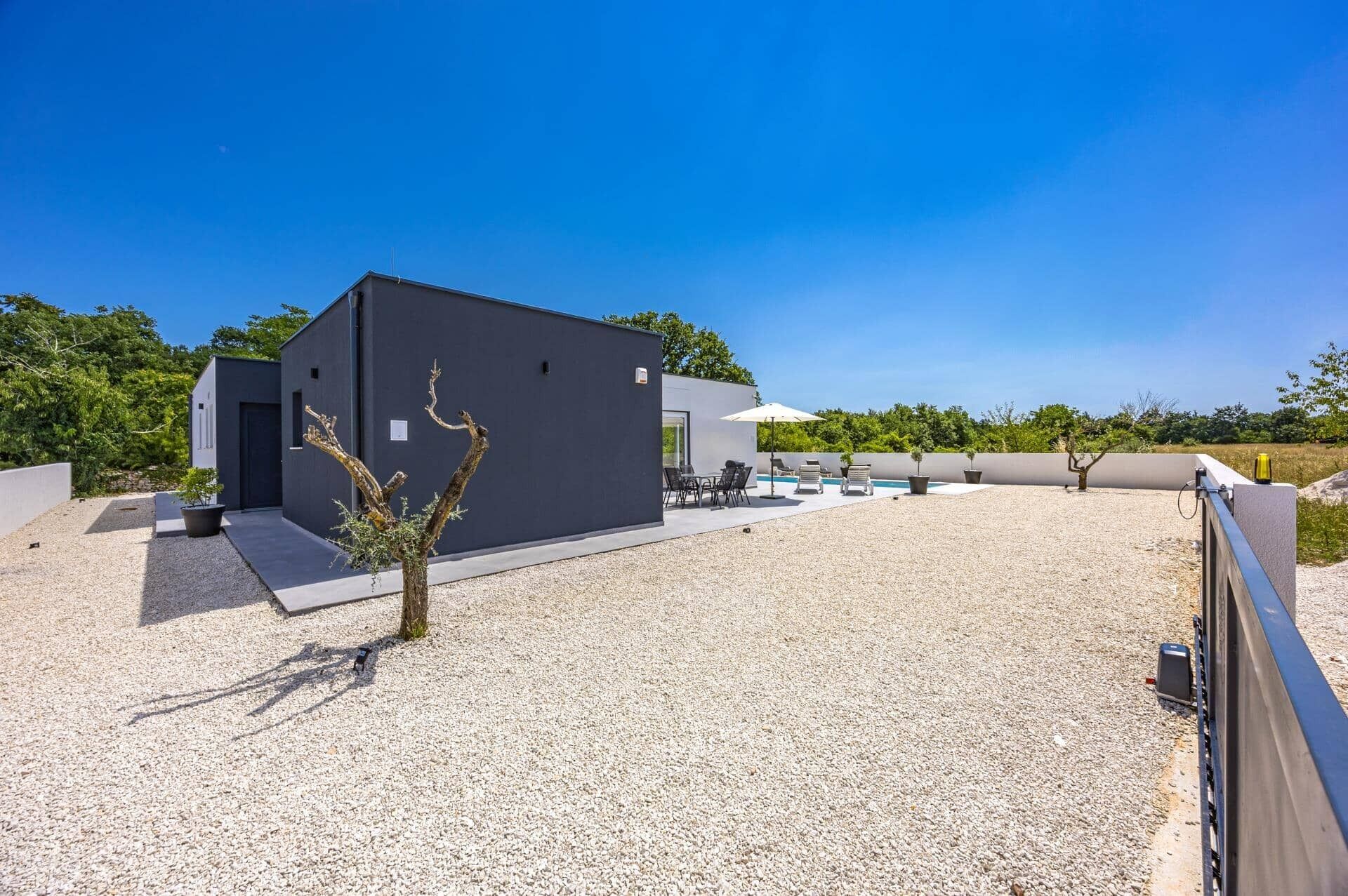 Een modern gebouw met een grindpad, terras en zwembad.