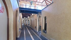 Un couloir doté d’un sol à carreaux, d’arcades et d’un balcon agrémenté de plantes.