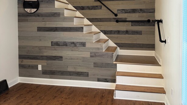 A staircase with a wooden finish and a black handrail, leading to a landing with a clock and a light fixture. - Delightful 2-bedroom fully remodeled house with AC in charming Oshkosh (Oshkosh)