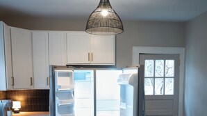 Una cocina moderna con armarios blancos, refrigerador empotrado y una lámpara colgante.