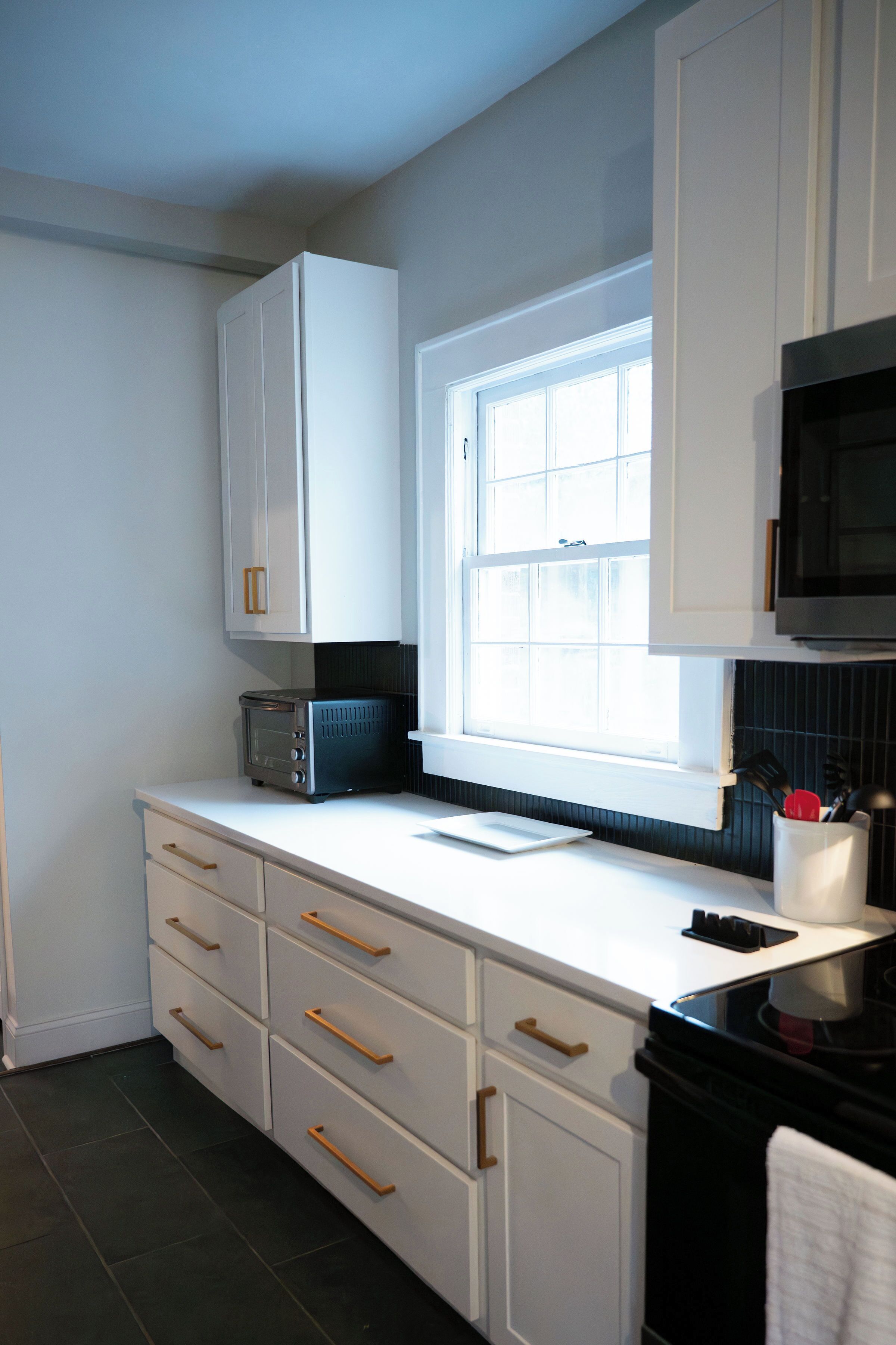 A kitchen with white cabinets, a microwave, a toaster, and a window.