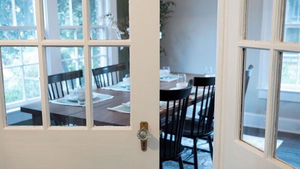 Una puerta blanca con un panel de vidrio, que da a un comedor con una mesa y sillas.