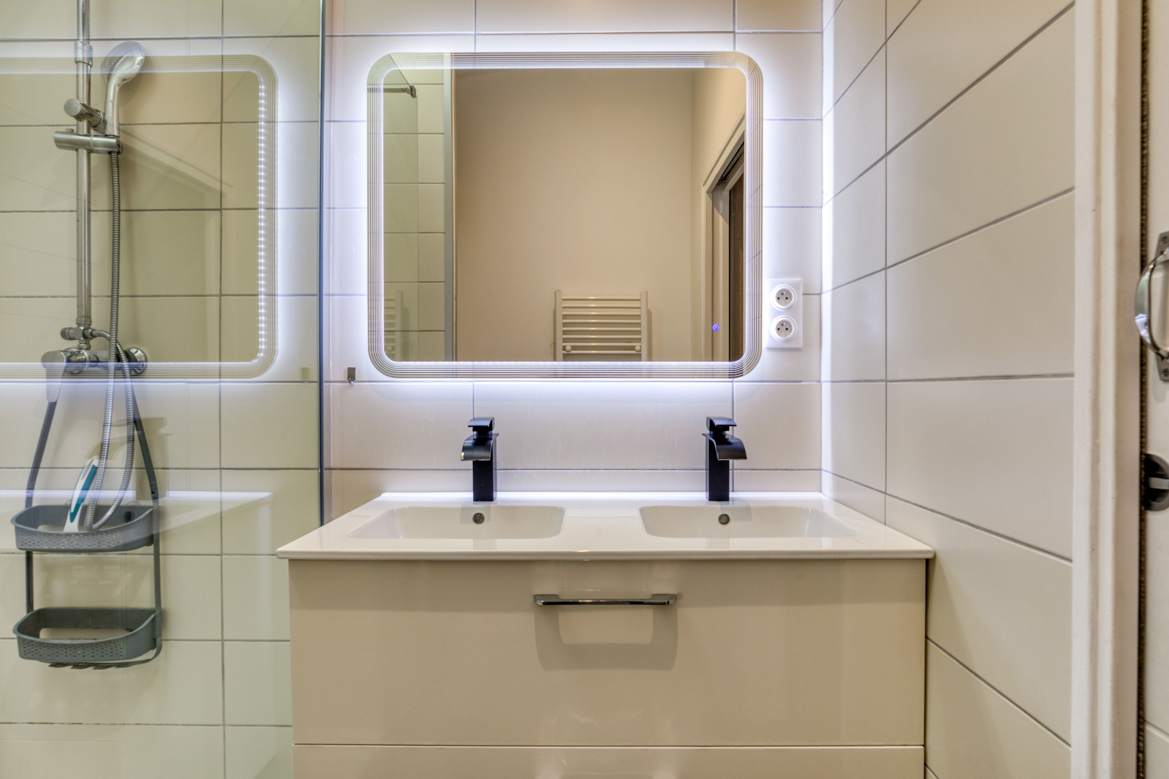 Ein Badezimmer mit einem Doppelwaschbecken, einem Spiegel und einer Dusche.