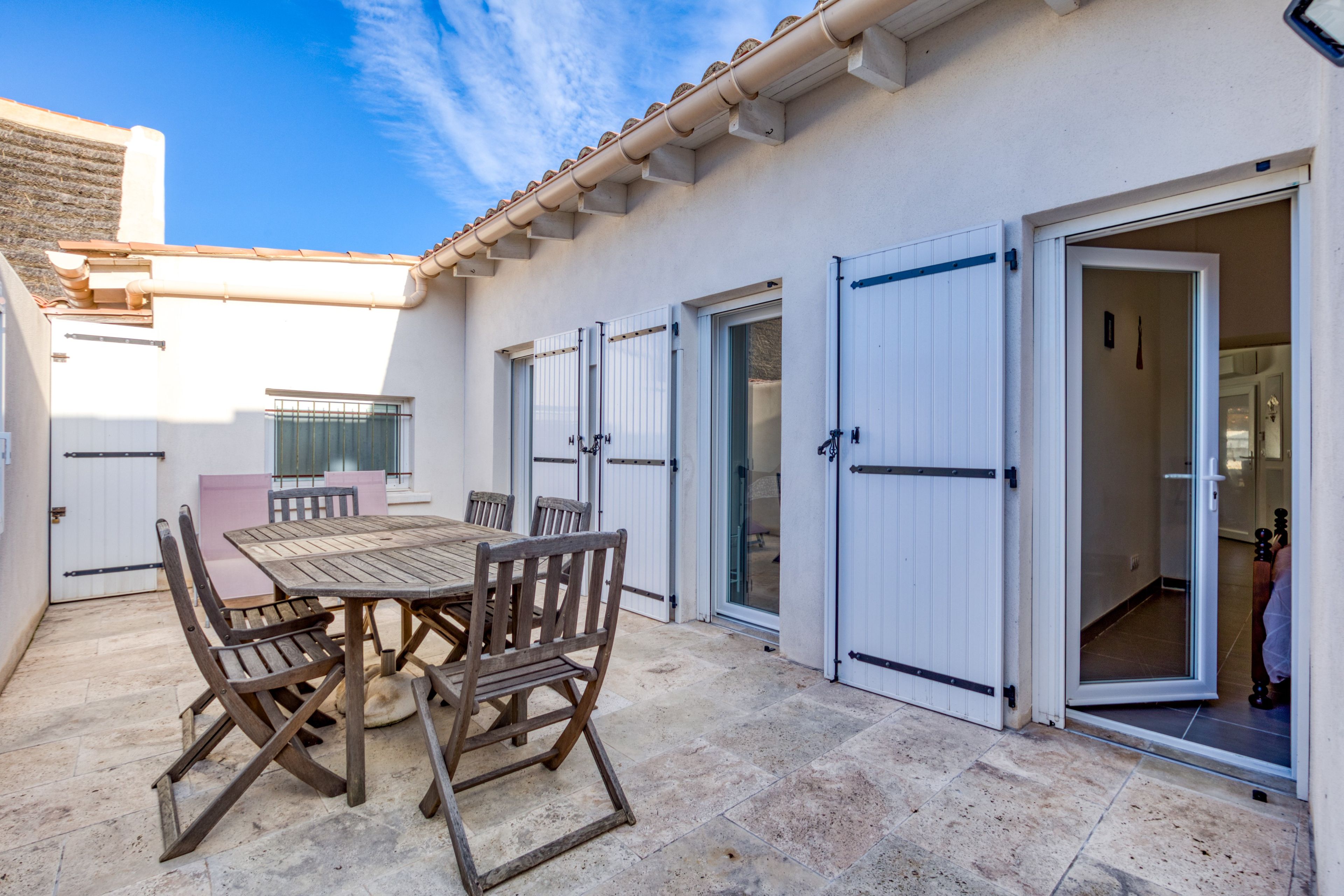 Un patio con una mesa y sillas de madera, una puerta blanca y un suelo de baldosas.