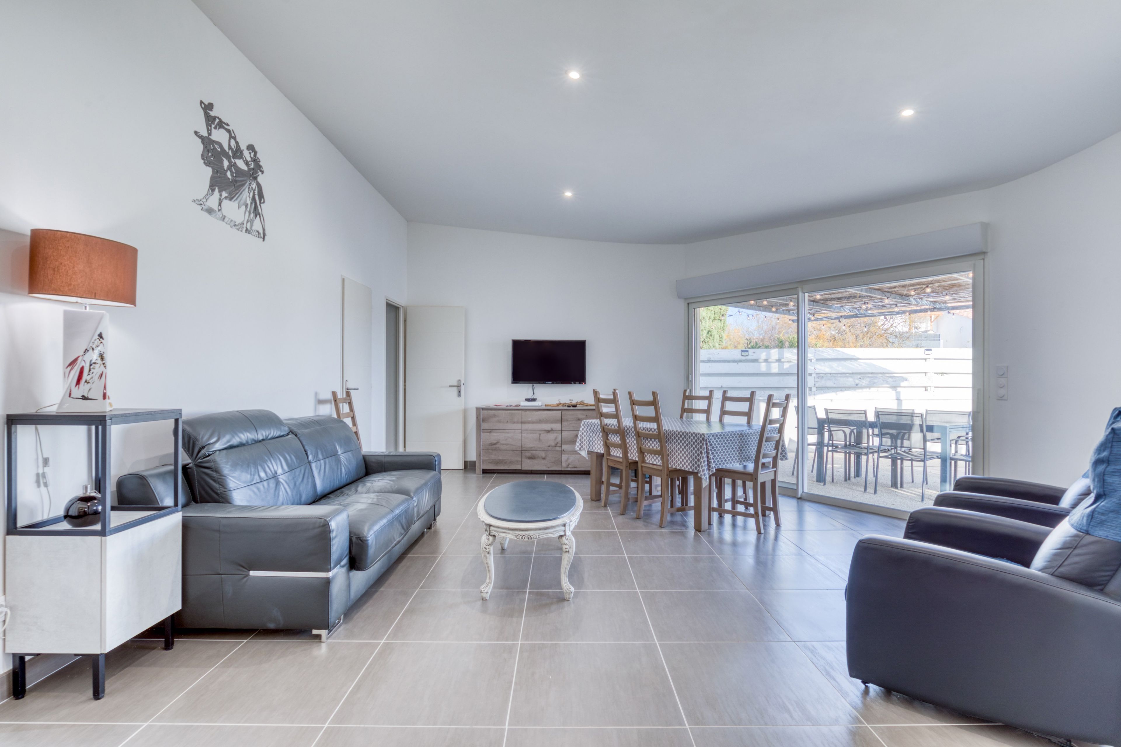 Een moderne woonkamer met een grijze bank, een salontafel en een eethoek met houten stoelen en een tafel.
