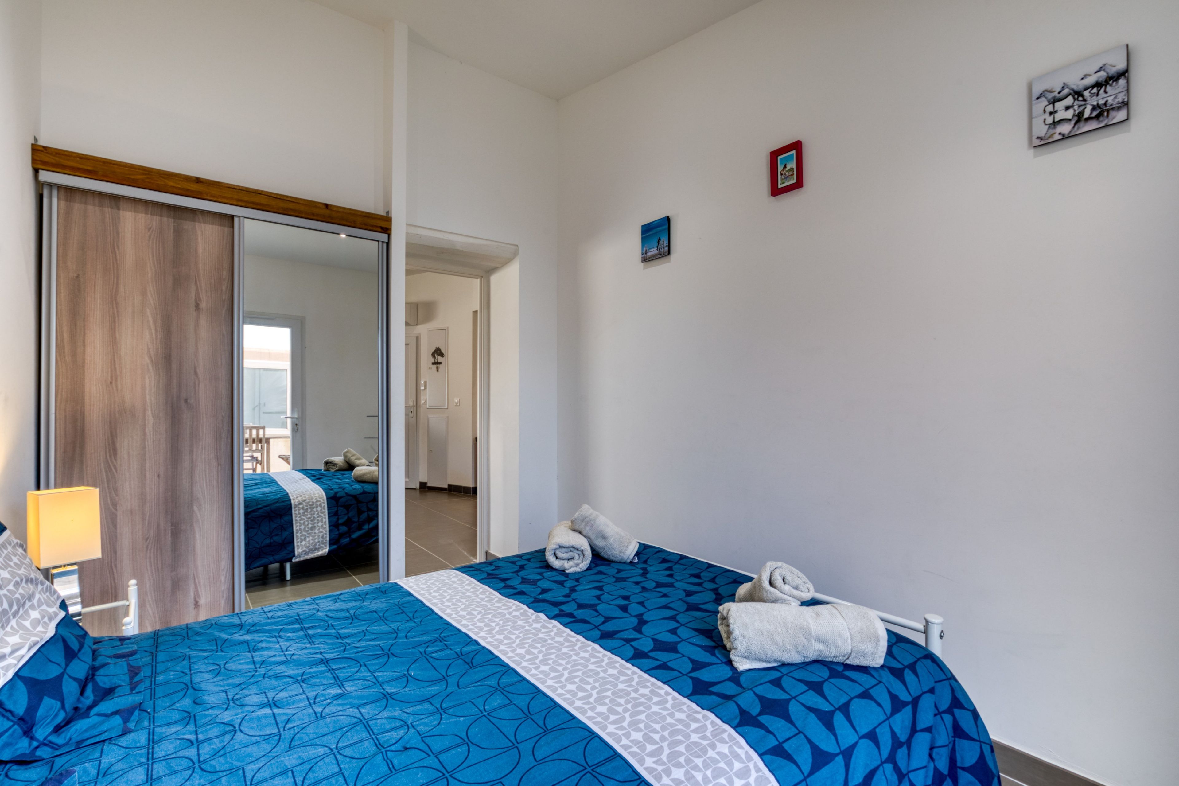 Een hotelkamer met een bed, een spiegel, een deur en een klein tafereel aan de muur.