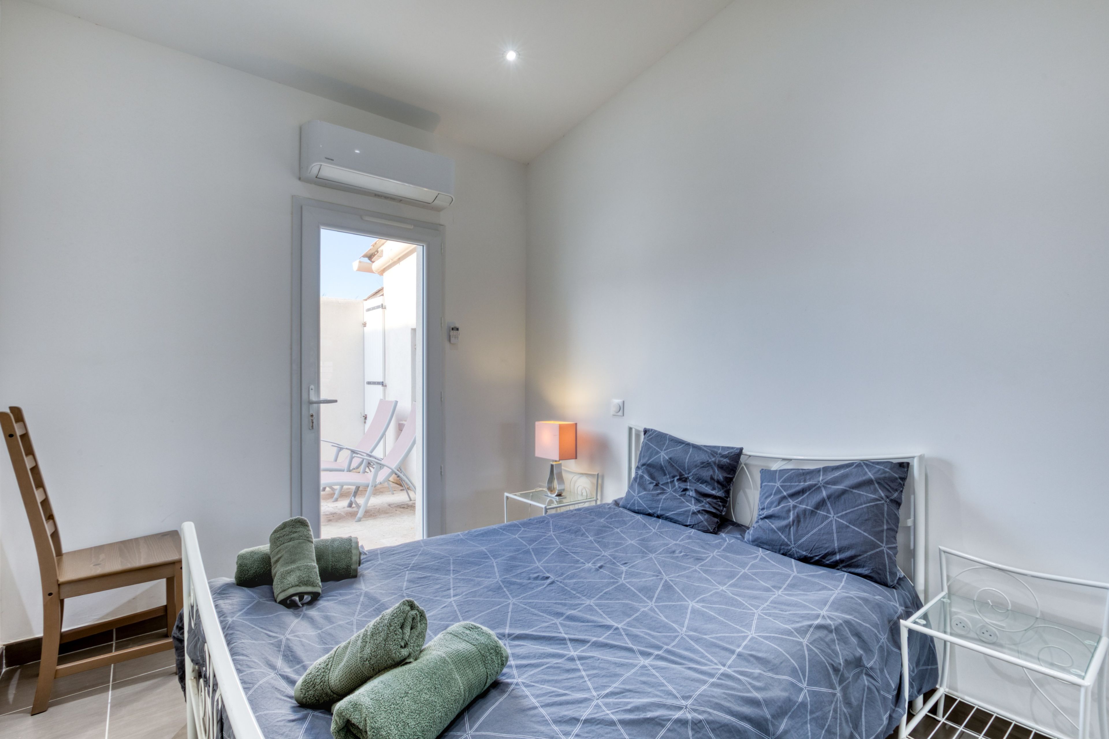 A bedroom with a bed, a chair, a lamp, and an air conditioning unit.