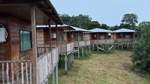 A row of wooden cabins with balconies, each elevated on stilts, surrounded by grass and trees. - Amazon tucuna ecologico  (Careiro)