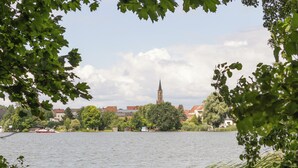 Een meer met een kerktoren in de verte, omringd door bomen en gebouwen.