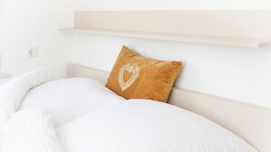 Een net opgemaakt bed met witte lakens en een enkel bruin kussen met een hartmotief.