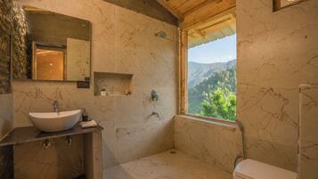 A bathroom with a marble sink, a toilet, and a shower. There is a window providing a view of the outdoors.