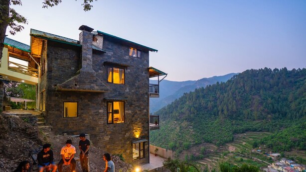 A stone building with multiple windows, a balcony, and a fire pit area. - Indulge Ramgarh Nainital by PACK (Kosiyakutoli)