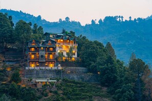 A multi-story hotel with balconies, located on a hillside with a mountainous backdrop. - Indulge Ramgarh Nainital by PACK (Kosiyakutoli)