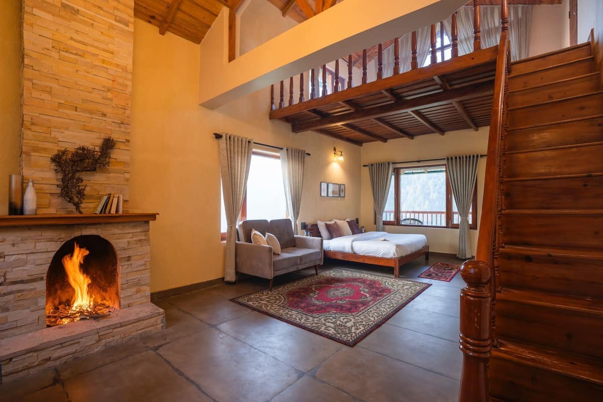 Un salón amplio con chimenea de piedra, un sofá, una cama y una escalera de madera.