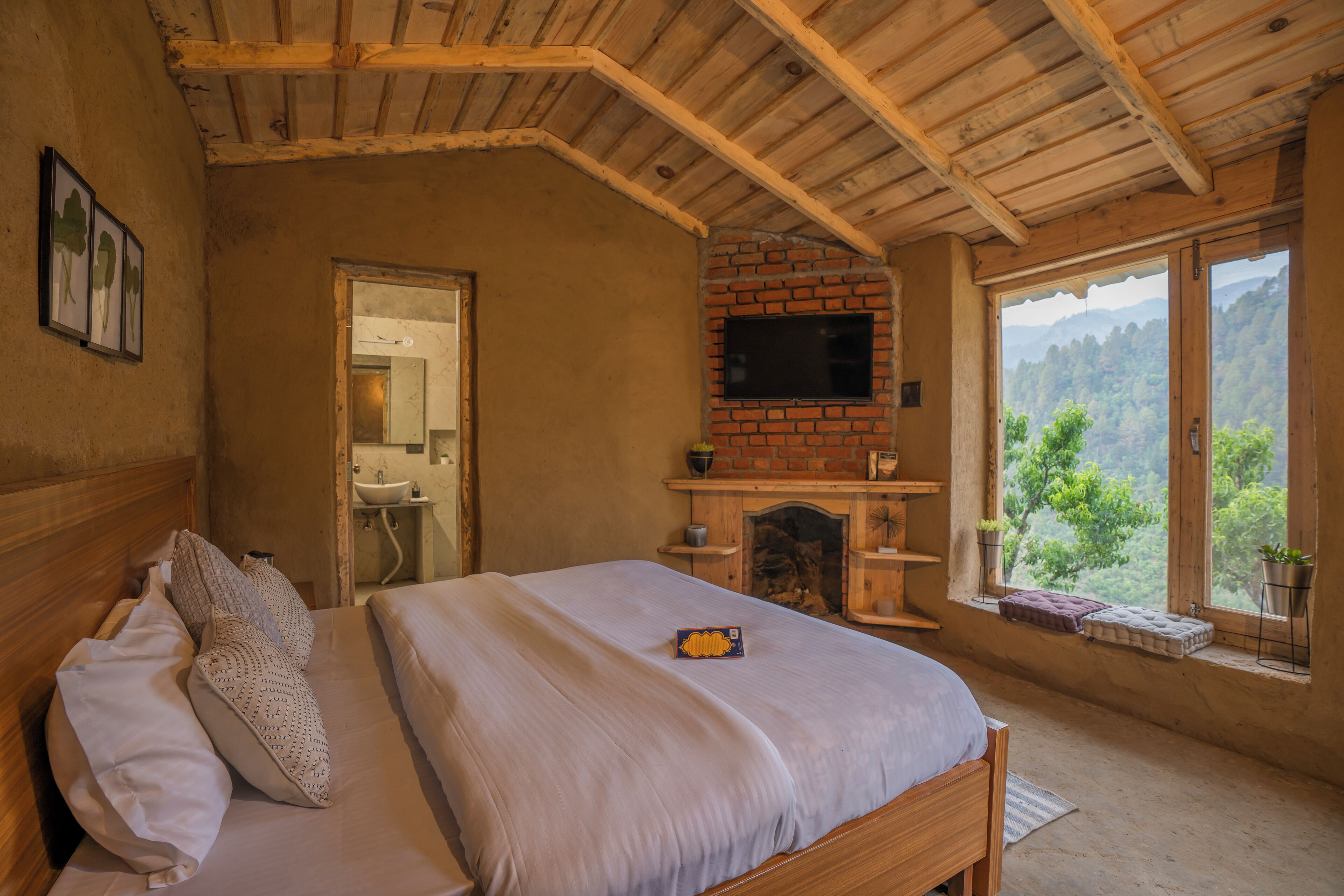 Un dormitorio con techo de madera, chimenea de ladrillo, cama con almohadas, mesita de noche y ventana con vistas a zonas verdes.