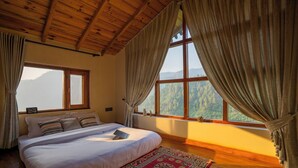 A bedroom with a large bed, wooden ceiling, and a view of a forest through a window. - Indulge Ramgarh Nainital by PACK (Kosiyakutoli)