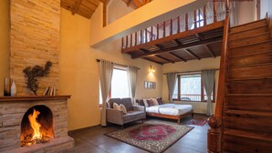 A spacious living room with a stone fireplace, a large bed, a sofa, and a wooden staircase. - Indulge Ramgarh Nainital by PACK (Kosiyakutoli)