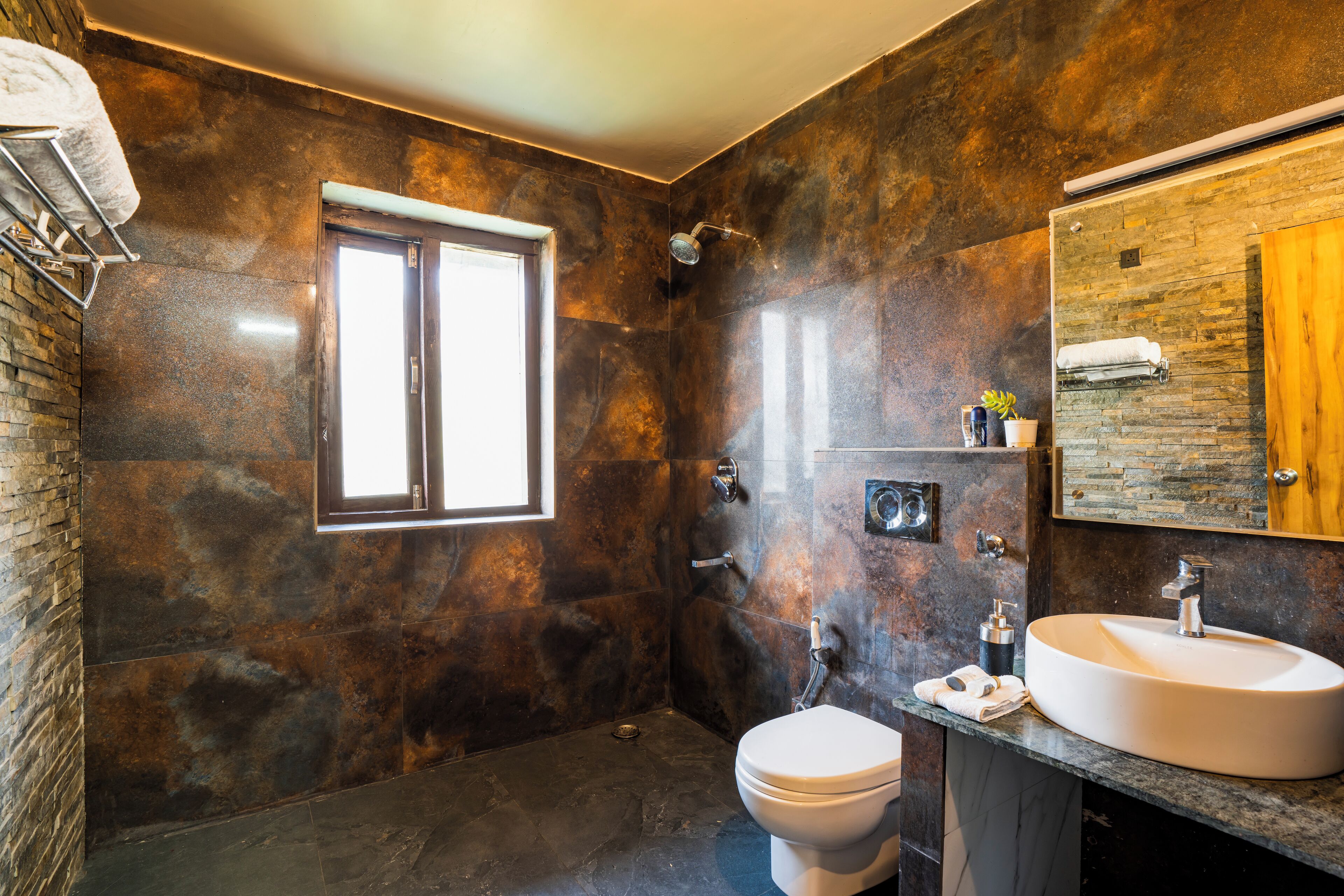 Une salle de bain moderne avec un mur en pierre, un grand miroir, un lavabo et des toilettes.