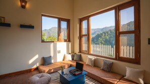 A cozy living room with a large window, a blue coffee table, and a sofa with cushions. - Indulge Ramgarh Nainital by PACK (Kosiyakutoli)