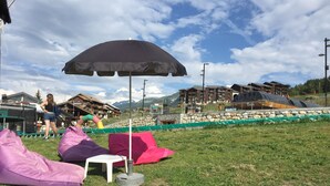 Ein Sitzbereich im Freien mit Sitzsäcken und einem Tisch unter einem großen Sonnenschirm, mit Blick auf Gebäude und Berge.