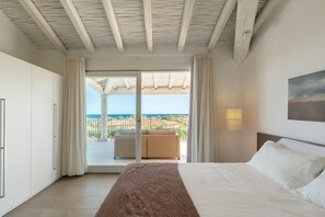 A bedroom with a large bed, a sliding glass door leading to a balcony with a view of the sea. - VILLA MELOGRANO - A blend of discreet elegance and total comfort, only 500 meters from Sardinia’s most stunning waters (Castiadas)