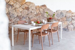 A dining table with four chairs, set with white plates, cups, and a basket of fruit. - VILLA MELOGRANO - A blend of discreet elegance and total comfort, only 500 meters from Sardinia’s most stunning waters (Castiadas)