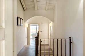 A hallway with a wooden railing, a tiled floor, and a white ceiling with exposed beams. - VILLA MELOGRANO - A blend of discreet elegance and total comfort, only 500 meters from Sardinia’s most stunning waters (Castiadas)